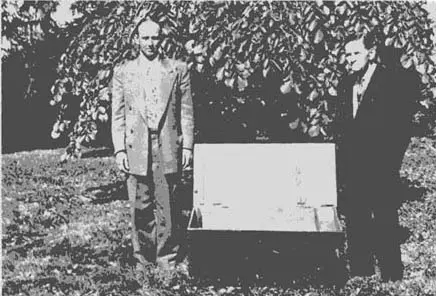 Two men standing next to a trunk in the grass.