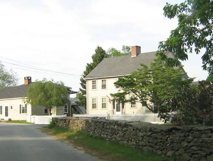 A house with a stone wall and trees in the background.